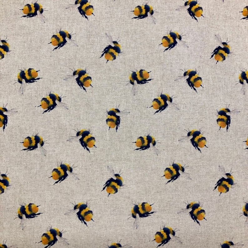 May include: A beige fabric with a repeating pattern of black and yellow bumblebees. The bees are flying in different directions.