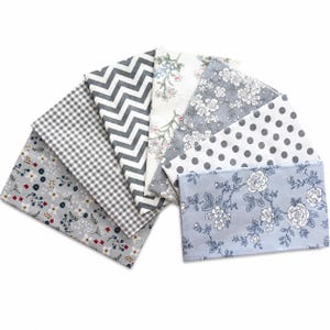 May include: A selection of fabric swatches featuring diverse patterns such as floral, polka dot, gingham, and chevron. The colour scheme is predominantly grey, white, and blue, with touches of red. The fabrics are arranged in a fan shape.