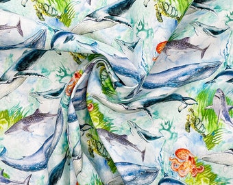 May include: A white fabric with a blue, green, and orange watercolor pattern of whales, fish, and sea turtles. The fabric is folded and shows the pattern repeating.