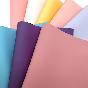 May include: A selection of colourful faux leather sheets in shades of pink, purple, blue, yellow, and white. The sheets are fanned out, displaying their smooth texture and vibrant colours. Suitable for various craft projects, offering a range of options.