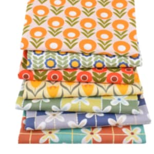 Op de afbeelding: Een stapel kleurrijke stoffen met bloemenpatronen. De stoffen hebben verschillende patronen met oranje, gele, blauwe en witte bloemen op verschillende gekleurde achtergronden. De stoffen zijn op elkaar gestapeld.