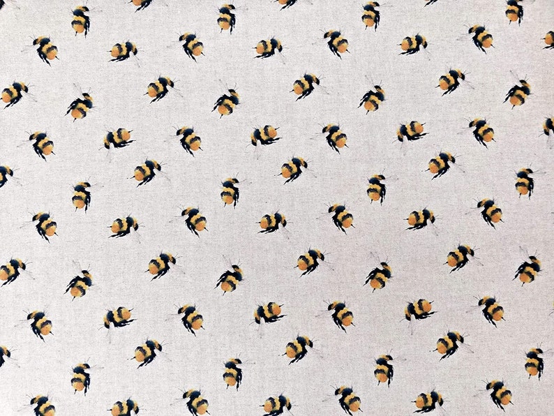 May include: A white fabric with a repeating pattern of yellow and black bumblebees. The bees are scattered randomly across the fabric.