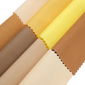Peut inclure: Gros plan sur une collection d'échantillons de tissu dans diverses nuances de jaune, marron et beige. Le tissu a un aspect légèrement texturé et est coupé avec un bord en zigzag. Les couleurs varient du crème clair au brun foncé.