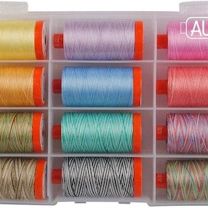 Può includere: Una scatola di plastica trasparente con dodici rocchetti di filo colorato. I colori del filo includono giallo, lavanda, rosa, arancione, azzurro, corallo, verde, verde acqua e marrone. Ogni rocchetto ha tappi arancioni e il logo Aurifil.