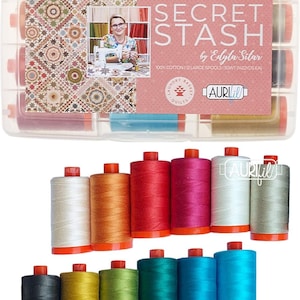 Może przedstawiać: Przezroczyste plastikowe pudełko z kolorowymi szpulkami nici. Pudełko ma różową etykietę z napisem "SECRET STASH by Edyta Sitar". Szpulki są w różnych kolorach, w tym czerwonym, różowym i niebieskim. Nić jest w 100% bawełniana.