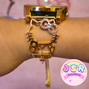 Op de afbeelding: Gouden horloge met een Hello Kitty-bedel. De bedel is versierd met roze en witte strass steentjes en een strik. De horlogeband is een gouden ketting.