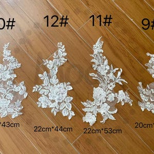 May include: Four white floral lace appliques with varying designs. Each applique is labeled with a number and size in centimeters. The appliques range in size from 20cm x 40cm to 25cm x 43cm.