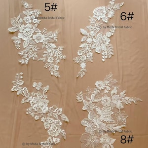 May include: Four white floral lace appliques with different designs are shown against a neutral backdrop. Each applique has detailed floral and leaf patterns. The numbers 5#, 6#, 7#, and 8# are printed on the image, along with the text "by Moda Bridal Fabric".