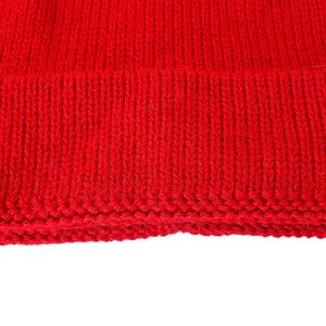 May include: A close-up of the bottom edge of a red knitted beanie hat. The hat is made of a soft, warm material and has a simple, classic design.