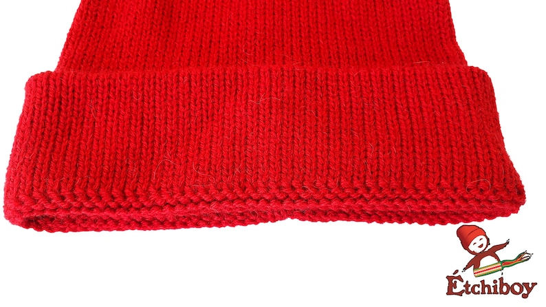 May include: A close-up of the bottom edge of a red knitted beanie hat. The hat is made of a soft, warm material and has a simple, classic design.