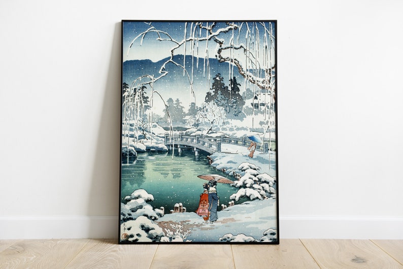 May include: A Japanese woodblock print depicting a snowy landscape with a bridge over a pond. Two figures in traditional clothing walk along the path, carrying umbrellas. The print is framed in black.