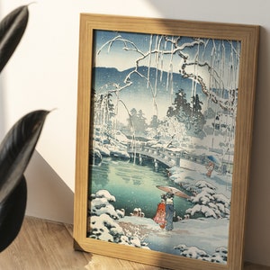 May include: A framed print of a Japanese woodblock print depicting a snowy landscape with a bridge over a pond. Two figures in traditional clothing walk along a path in the snow.