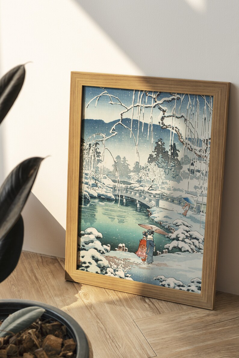 May include: A framed print of a Japanese woodblock print depicting a snowy landscape with a bridge over a pond. Two figures in traditional clothing walk along a path in the snow.