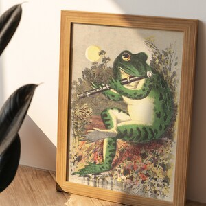 K&ouml;nnte beinhalten: Eine gerahmte Illustration eines gr&uuml;nen Frosches, der in einer Waldlandschaft Fl&ouml;te spielt. Der Frosch sitzt mit gekreuzten Beinen und geschlossenen Augen auf einem Stein. Der Hintergrund ist ein &uuml;ppiger gr&uuml;ner Wald mit einem leuchtend gelben Mond am Himmel.