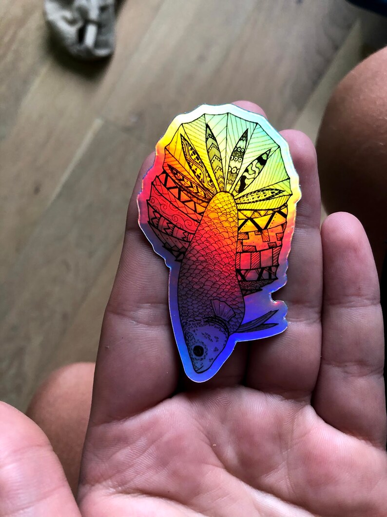 Puede incluir: Una pegatina hologr&aacute;fica de un pez con un dise&ntilde;o intrincado en blanco y negro. El pez est&aacute; delineado en negro y tiene un degradado de colores de rojo a azul.