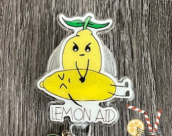May include: A clear plastic badge reel with a yellow lemon design. The lemon has a face and is holding a smaller lemon. The text "LEMON AID" is printed on the reel. The reel is attached to a metal chain with a yellow lemon charm.
