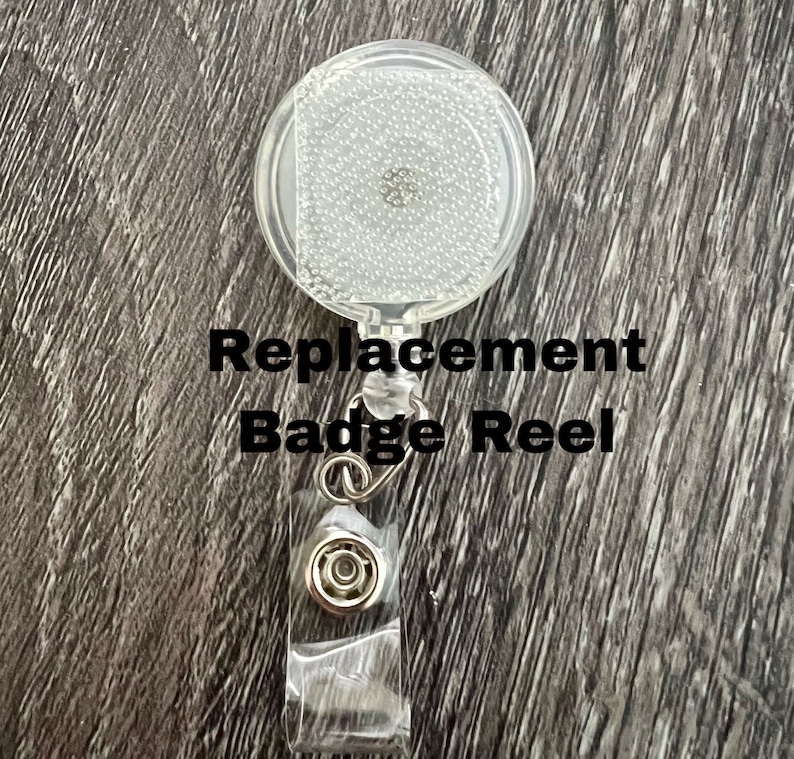 Peut inclure: Un porte-badge en plastique transparent avec un cordon r&eacute;tractable argent&eacute; et un clip argent&eacute;. Le porte-badge est dot&eacute; d'un couvercle en plastique transparent avec une surface textur&eacute;e. Le texte "Replacement Badge Reel" est imprim&eacute; en noir sur fond blanc.