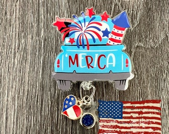 May include: A blue and red 'Merica' themed retractable badge holder with a red, white, and blue heart charm and a red, white, and blue American flag charm. The badge holder has a blue truck bed with fireworks and a red, white, and blue firecracker. The badge holder is attached to a clear plastic badge holder with the text 'V-spin Designs Creative Crafts'.
