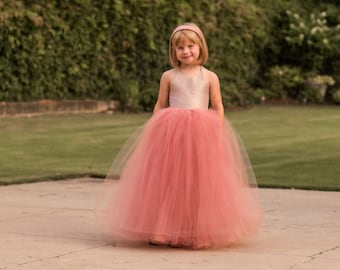 May include: A young girl wearing a pink tulle dress with a satin bodice. She is standing on a paved surface with a green lawn in the background.