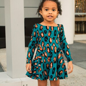 May include: A young girl wearing a teal blue dress with a brown and black leopard print. The dress has long sleeves and a flared skirt.