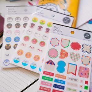 Puede incluir: Un conjunto de tres hojas de pegatinas coloridas con varios diseños. La primera hoja presenta pingüinos de dibujos animados, la segunda hoja presenta animales de dibujos animados y la tercera hoja presenta formas coloridas, pancartas y etiquetas con los días de la semana, listas de tareas, listas de deseos y etiquetas de eventos. El texto en las hojas de pegatinas dice "Point Sticker" y "マスキングテープ材32".