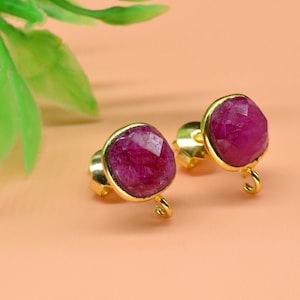 May include: A pair of gold earrings with pink gemstone accents. The earrings have a small hook closure.