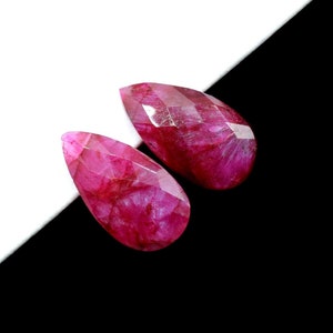 May include: Two teardrop-shaped pink gemstones with a faceted cut. The gemstones are on a black and white background.