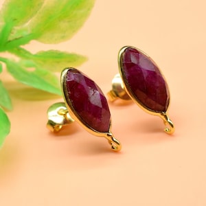 Pode incluir: Um par de brincos de ouro com detalhes de pedras preciosas vermelhas. Os brincos têm a forma de uma lágrima e são adornados com uma única pedra preciosa vermelha em cada brinco.