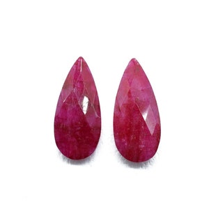 May include: Two pear-shaped ruby gemstones, each with a faceted cut and a deep red colour.