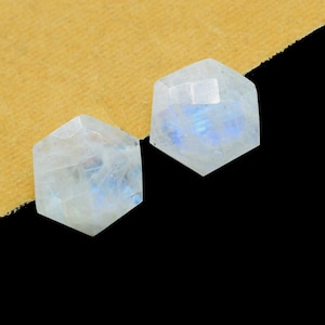 May include: Two iridescent white moonstone cabochons, cut into hexagonal shapes, with a blue sheen.