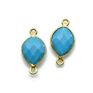 Pode incluir: Dois pingentes de conexão dourados com detalhes de pedras preciosas facetadas azul turquesa. Os pingentes têm dois laços de cada lado para serem presos a joias.