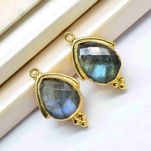 May include: Two gold-tone teardrop-shaped pendants with a blue-green labradorite gemstone. Each pendant has a small gold bead detail at the bottom.