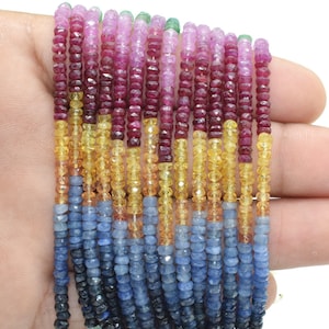 Op de afbeelding: Een streng facetgeslepen edelsteen kralen in tinten blauw, geel, roze en rood. De kralen zijn geregen op een doorzichtige draad en zijn ongeveer 4 mm in diameter.