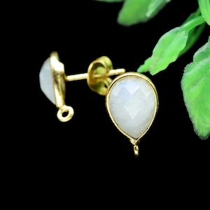 May include: A pair of gold-tone earrings with teardrop-shaped white moonstone stones. The earrings have a simple design and are perfect for everyday wear.