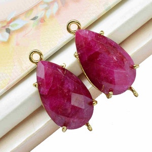 May include: Two teardrop-shaped ruby red gemstone pendants with gold-toned jump rings and prongs.