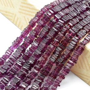 Puede incluir: Primer plano de hebras de piedras preciosas rectangulares de color púrpura intenso. Las cuentas están ensartadas, creando una superficie texturizada. Las piedras preciosas tienen un aspecto pulido y se muestran sobre un fondo claro.