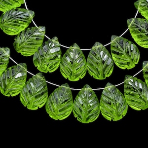 May include: A strand of green glass beads shaped like leaves. The beads are faceted and have a textured surface.