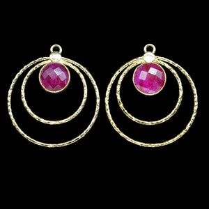 May include: A pair of gold hoop earrings with a pink gemstone in the center of each hoop. The hoops have a textured finish and are layered.