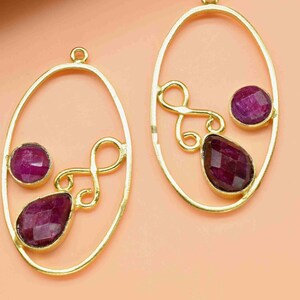 Puede incluir: Un par de bases de pendientes ovaladas de oro con un diseño de espiral decorativo y tres piedras preciosas moradas.