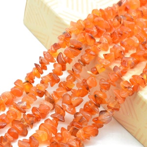May include: A strand of orange carnelian chip beads. The beads are irregular in shape and have a natural, polished finish.