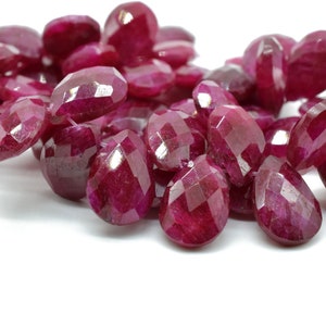 May include: A pile of faceted ruby gemstones in a deep red colour. The stones are oval shaped and have a smooth, polished finish.
