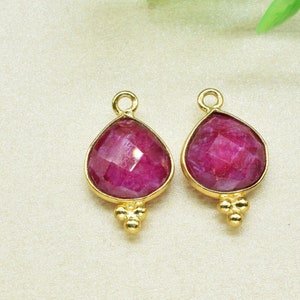 Puede incluir: Dos colgantes de tono dorado con una piedra preciosa de color rojo rubí en forma de lágrima. Cada colgante tiene un bucle en la parte superior para sujetarlo a un collar o pulsera.