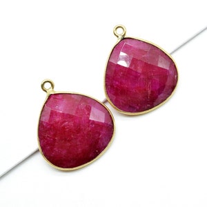 Könnte beinhalten: Zwei tropfenförmige Anhänger aus rubinrotem Edelstein mit goldfarbenen Zargen und Sprungringen.