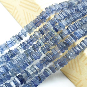 May include: A strand of blue gemstone beads, each bead is a rectangular prism with a slightly irregular shape. The beads are arranged in a line and are strung together with a clear thread.