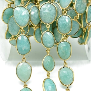 May include: A gold chain with light blue, faceted, oval-shaped gemstones. The chain is wound around a spool.