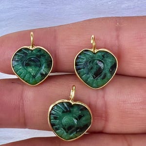 May include: Three gold-plated heart-shaped pendants with green jade inlays. The pendants feature a detailed carved design.