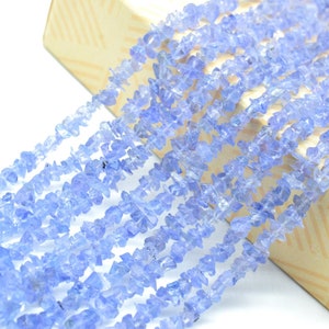 May include: A strand of light blue gemstone chips, arranged in rows, on a beige background. The chips are irregular in shape and have a translucent appearance.