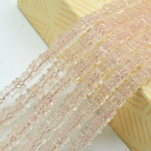 Könnte beinhalten: Eine Strähne aus hellrosa, facettierten, quadratischen Perlen. Die Perlen sind auf einem durchsichtigen Faden aufgefädelt und in einem versetzten Muster angeordnet.