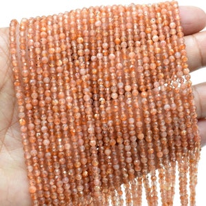 May include: A strand of sunstone beads, with a warm orange-brown color and a shimmery, iridescent finish. The beads are round and have a slightly faceted appearance.