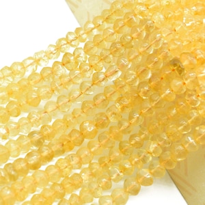 Puede incluir: Primer plano de hebras de cuentas facetadas de citrino amarillo dorado. Las cuentas están ensartadas, creando un efecto texturizado y luminoso. Las cuentas son de un color cálido y soleado, perfectas para la fabricación de joyas.